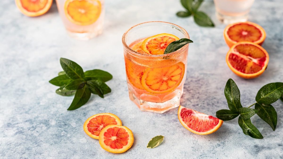 ein Glas Martini Tonic mit Grapefruit-Scheiben darin, daneben liegen Grapefruits und Minze.