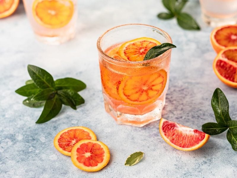 ein Glas Martini Tonic mit Grapefruit-Scheiben darin, daneben liegen Grapefruits und Minze.