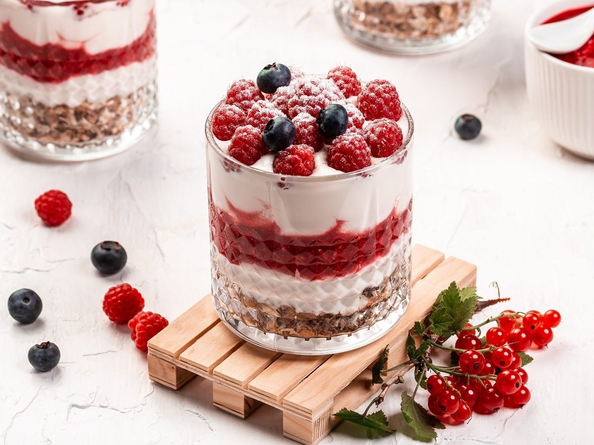 Ein Glas mit Himbeer-Cheesecake im Glas neben frischen Beeren