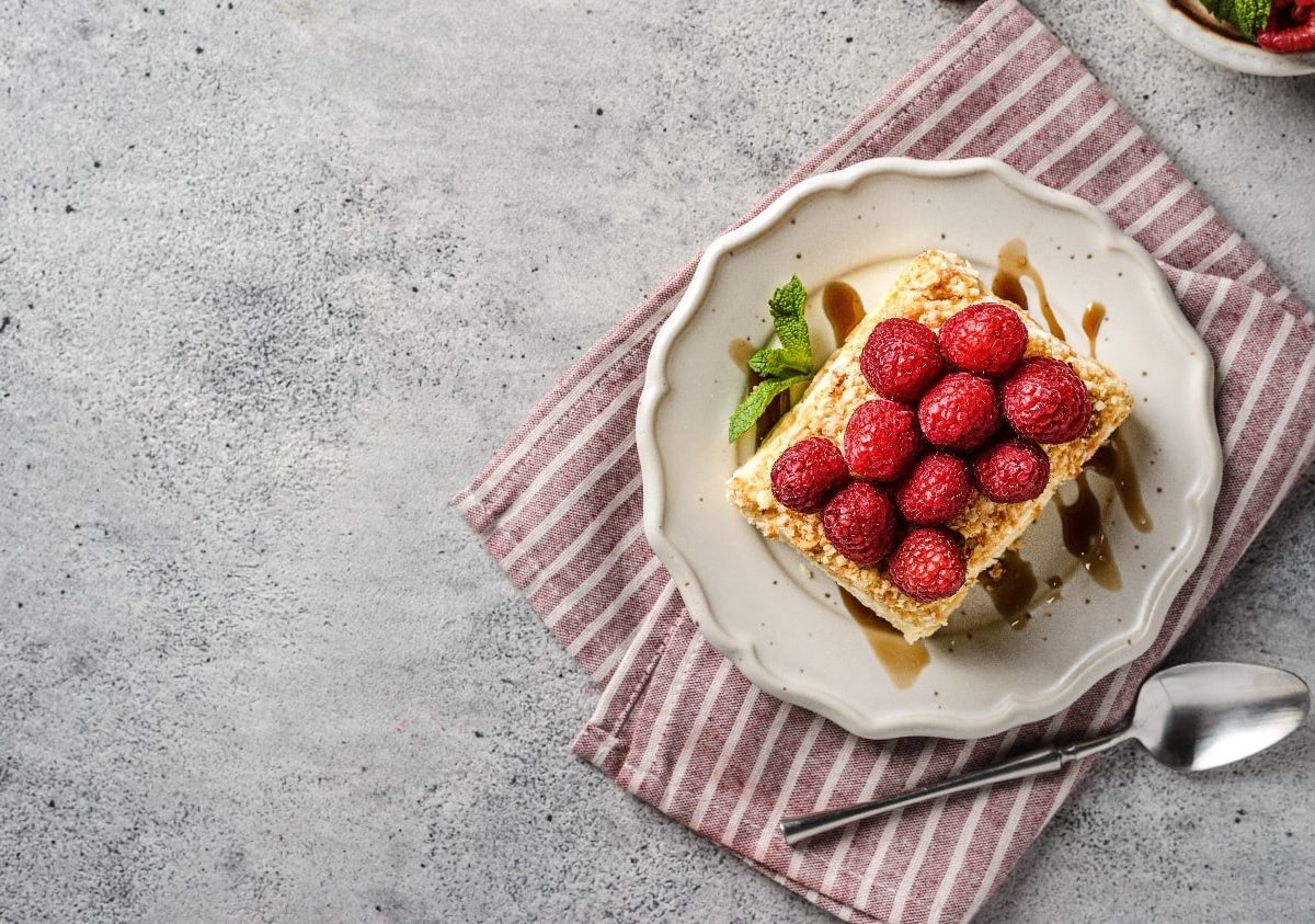 Ein Stück Napoleon-Torte auf einem weißen Teller mit einer rot-weiß-gestreiften Tischdecke auf einem grauen Tisch.