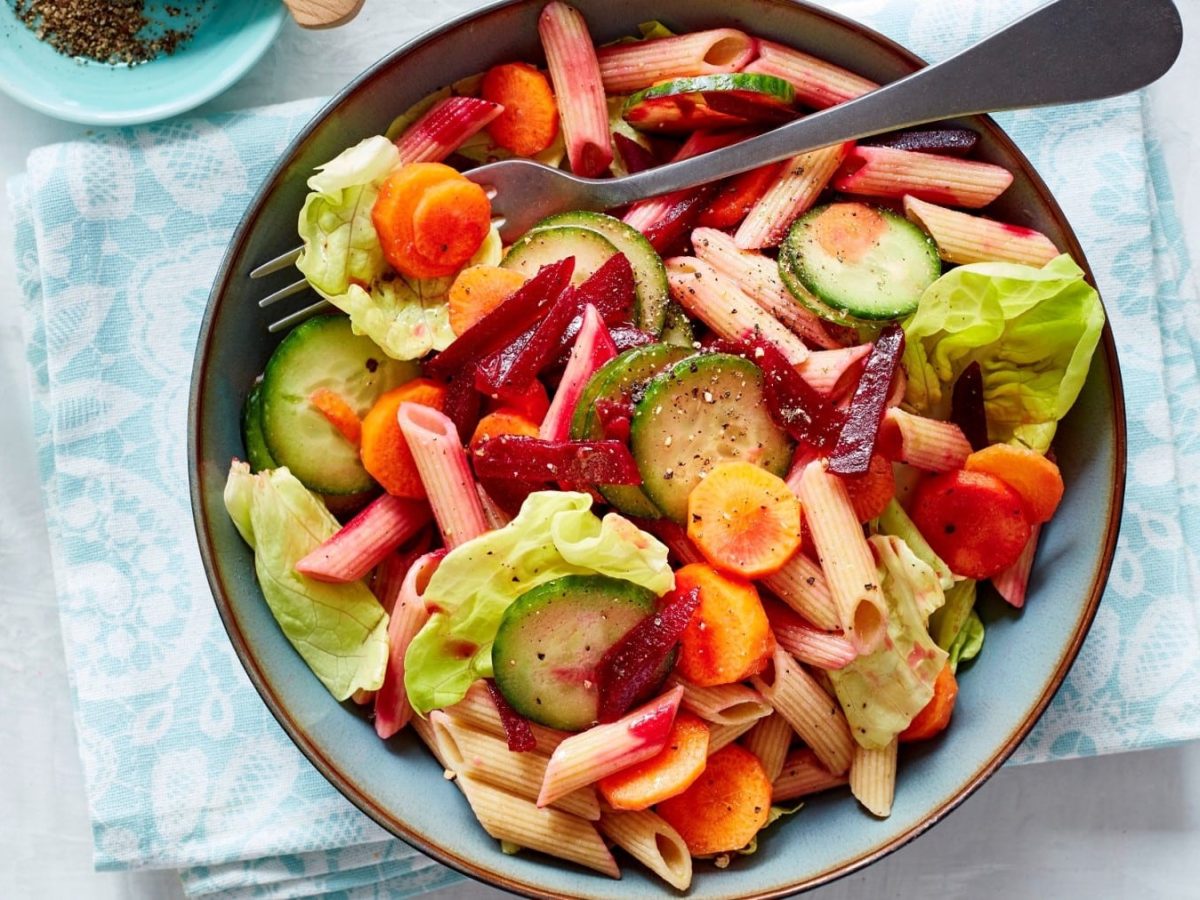 Nudelsalat mit Rote Bete in einer blauen Schüssel auf einem blauweißen Küchentuch.