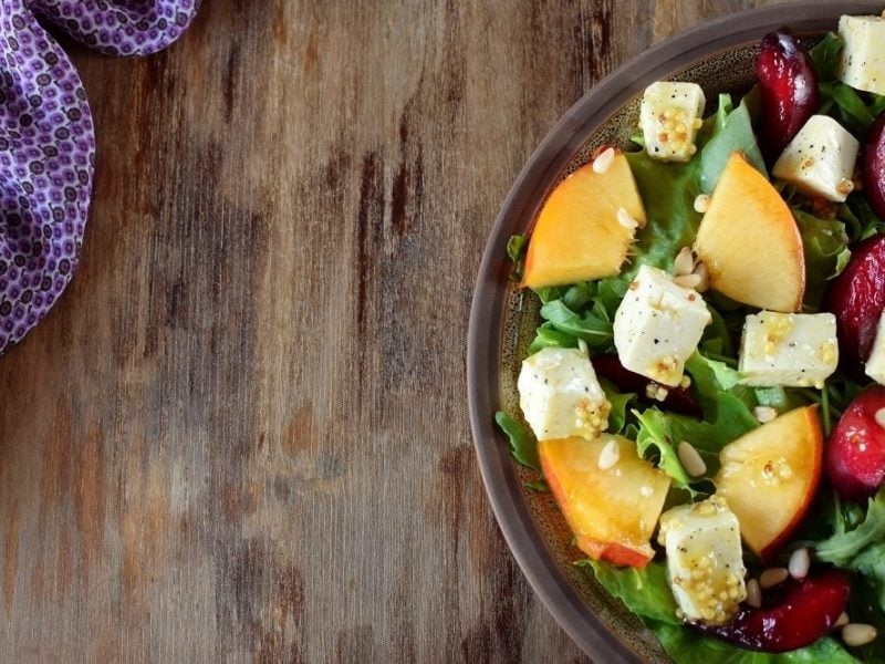 Ein Teller Obstsalat mit Rucola, Nektarinen und Pflaumen steht auf einem Tisch. Daneben liegt ein Tuch.