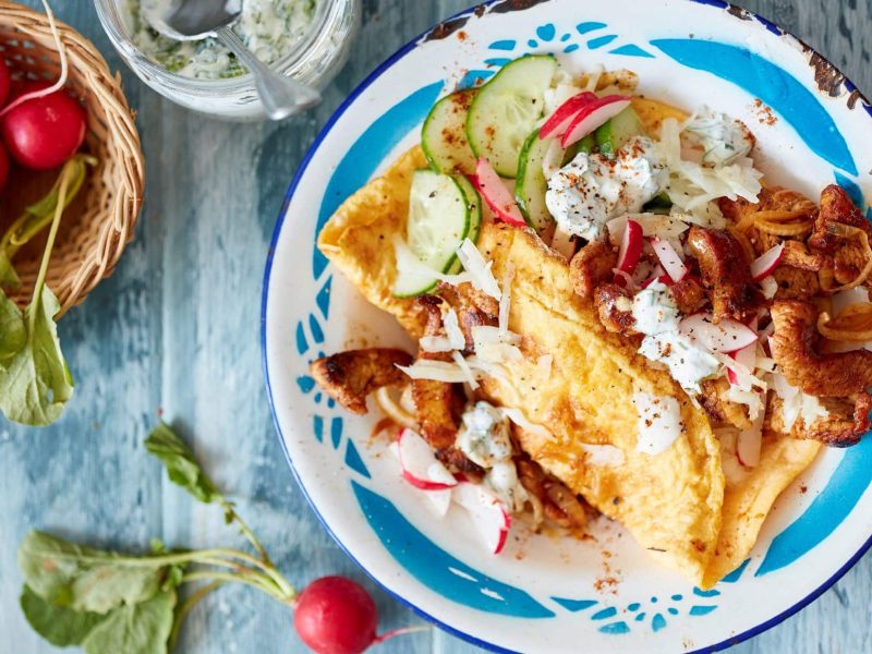 Ein Omelett-Döner liegt auf einem weiß-blauen Teller. Daneben befinden sich verschiedene Zutaten.