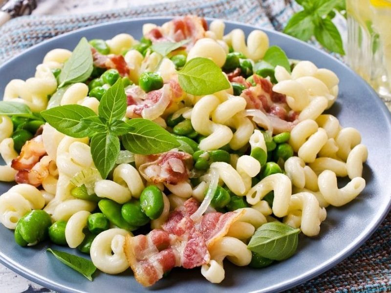 ein Teller Pasta mit Zwiebeln, Bohnen und Speck steht auf einem Tuch.