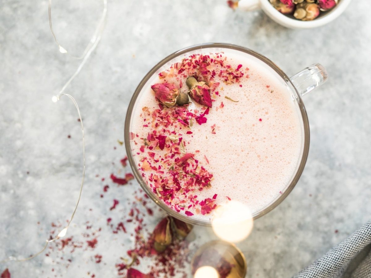 Pink Ayurveda Latte in einem Glas. Daneben stehen verschiedene Zutaten.