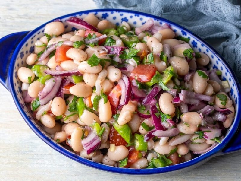 eine schale mit dem türkischen salat Piyaz steht auf einem weißen untergrund.