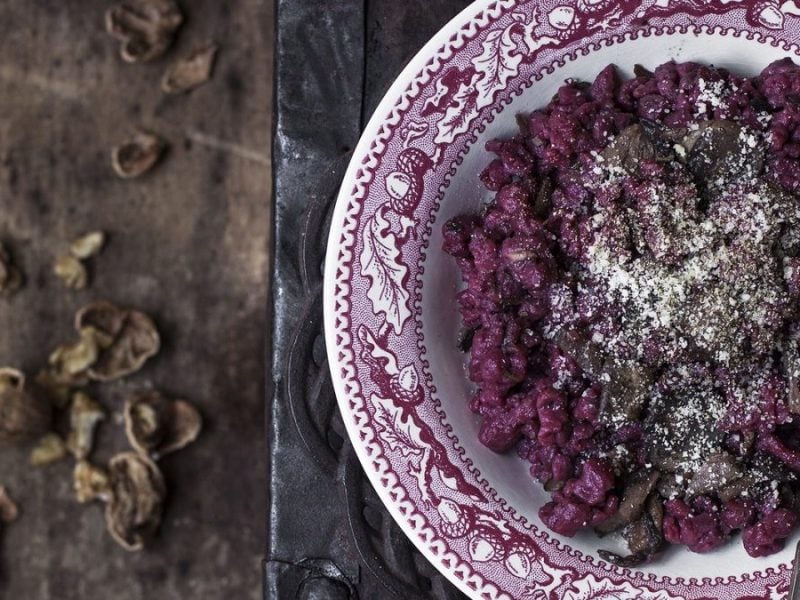 Ein Teller Rote-Bete-Spätzle mit Nüssen und Parmesan steht auf einem dunklen Tisch.