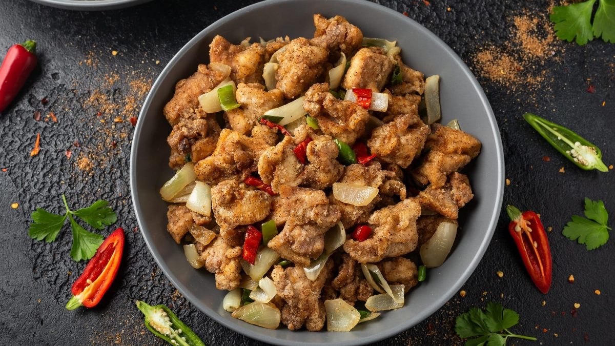 Ein runder Teller mit Salt and Pepper Chicken neben frischen Chilischoten.