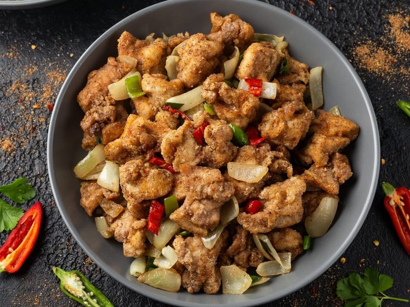 Ein runder Teller mit Salt and Pepper Chicken neben frischen Chilischoten.