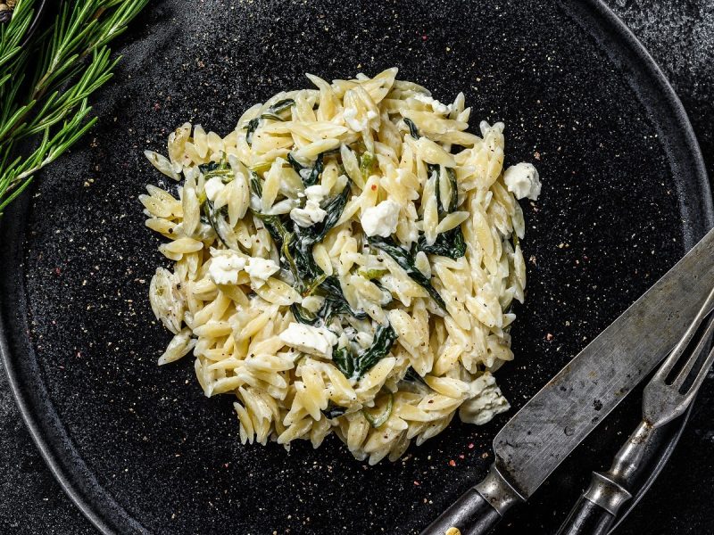 Ein schwarzer Teller mit Orzo-Pasta mit Spinat und Ricotta.