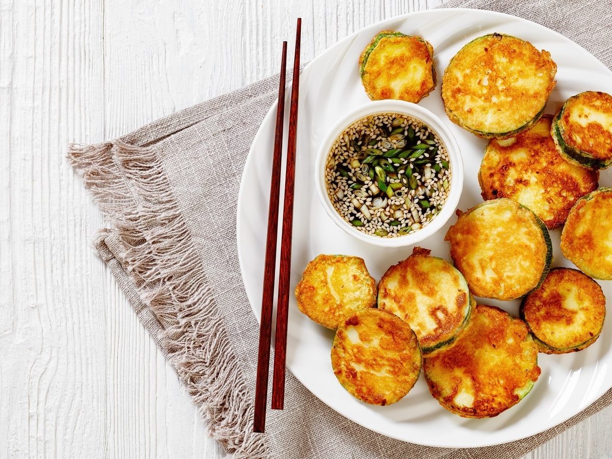 Ein weißer Teller mit Hobak Jeon auf einem braunen Geschirrtuch.