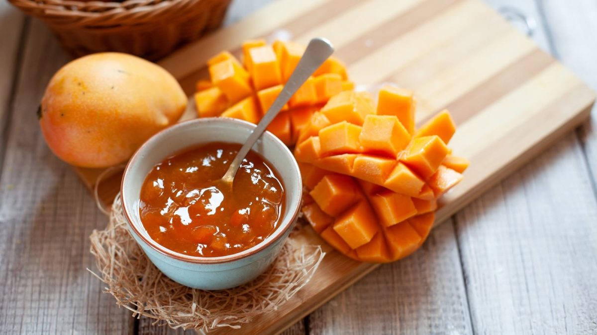 Eine Schüssel mit Solero Marmelade neben frischer Mango auf einem Holzbrett