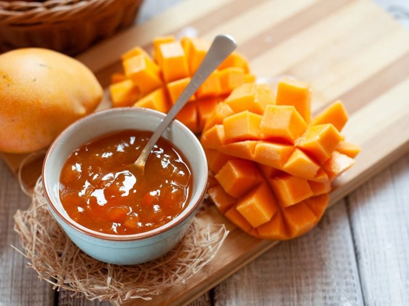 Eine Schüssel mit Solero Marmelade neben frischer Mango auf einem Holzbrett