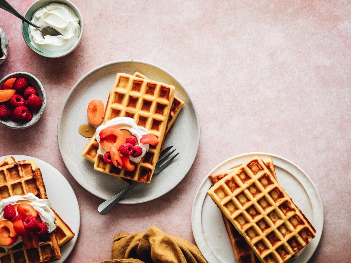 Tag der Waffel: Drei Teller mit Waffeln, Schlagsahne und frischem Obst in der Draufsicht.