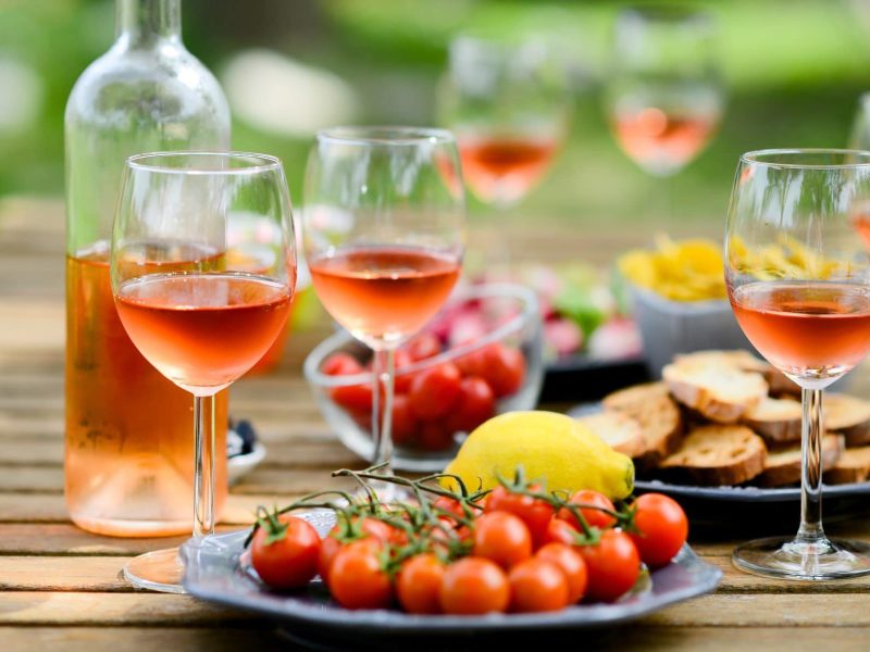 Zum Tag des Rosé Gläser und Flasche mit Rosé auf Picknicktisch im Freien.
