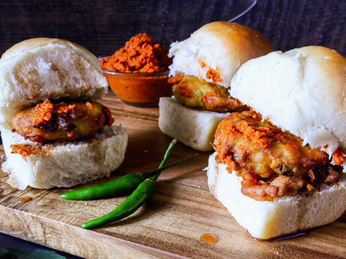 Vada Pav indischer Street Food Burger aus Kartoffeln, vegan, mit grünen Chilis, Paste in einer Schale auf Holzbrett. Frontalansicht.