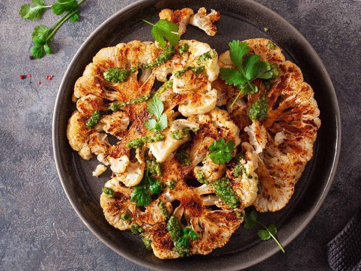 Ein Teller mit veganen Blumenkohlschnitzeln und frischen Kräutern in der Draufsicht.