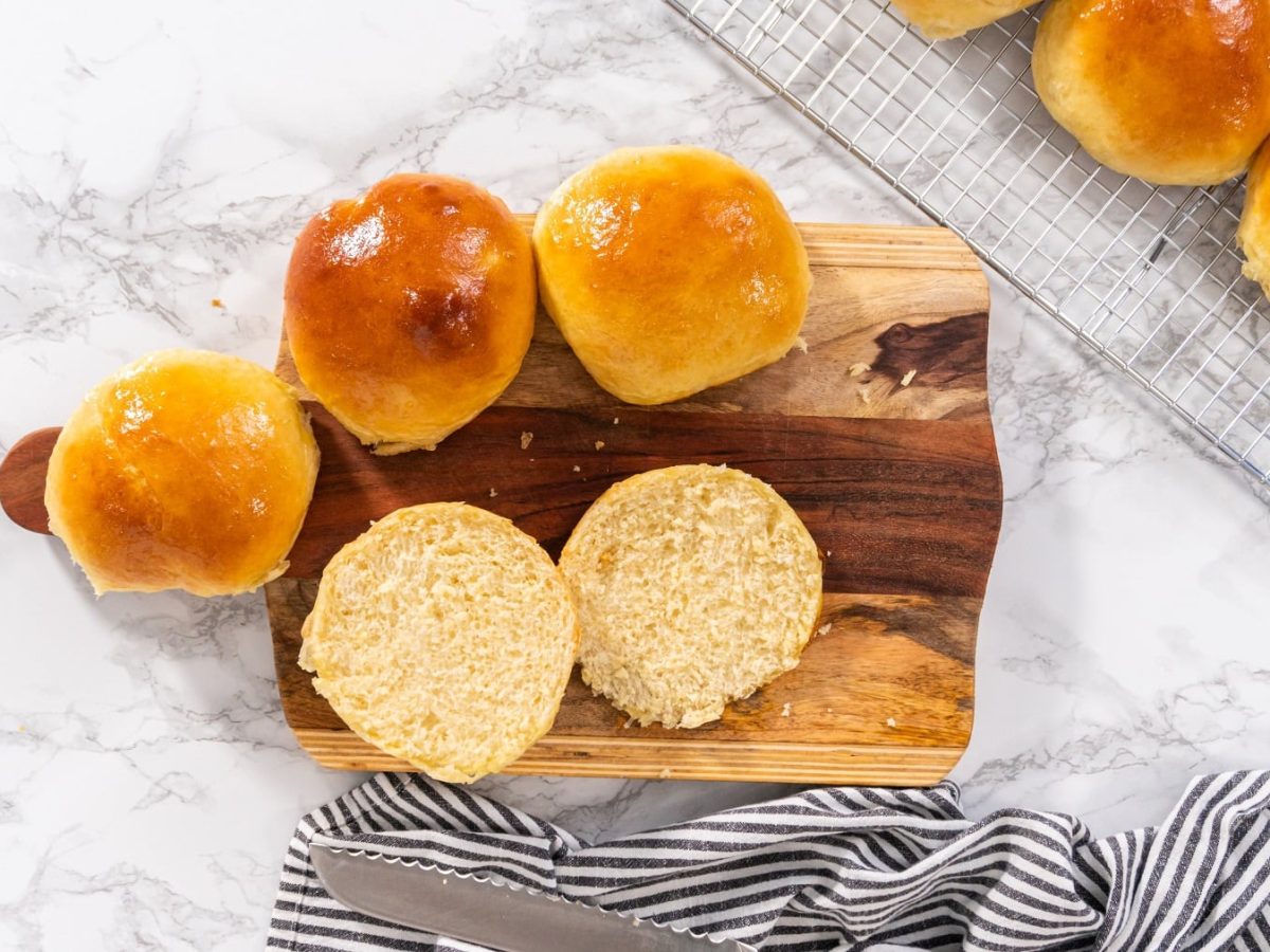 vegane Brioche-Brötchen auf einem Holzbrett und einem Gitter in der Draufsicht, eins davon ist aufgeschnitten.