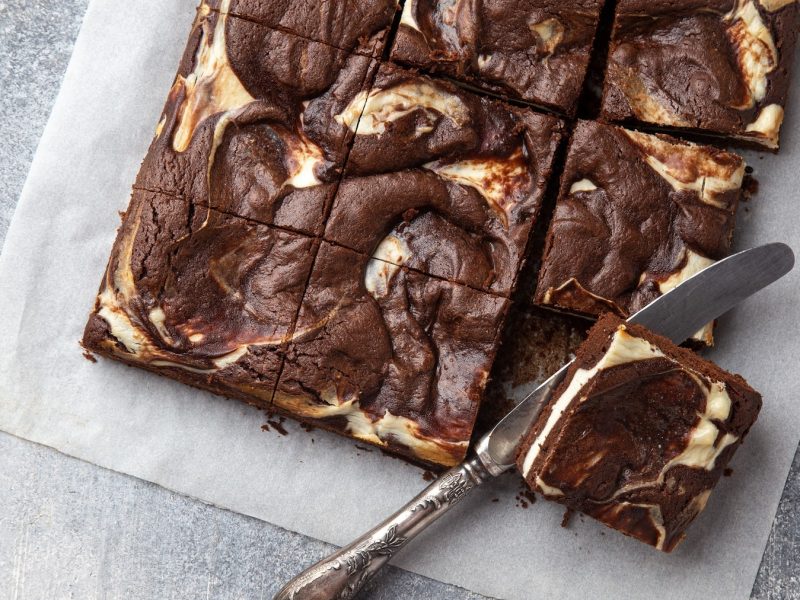 vegane Cheesecake Brownies auf einem Stück Backpapier in der Draufsicht, daneben ein Messer.