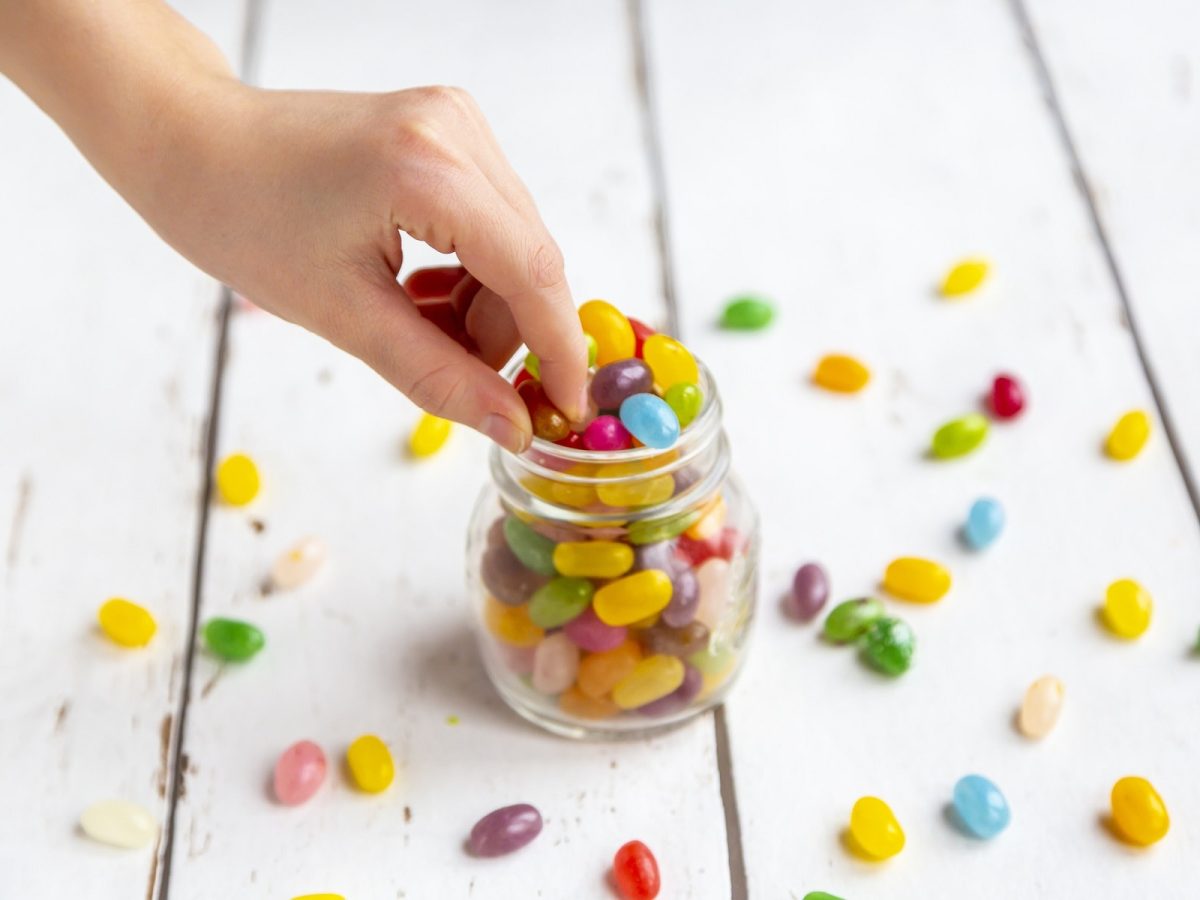 Vegane Süßigkeiten: ein Glas mit Fruchtgummi-Bohnen, in das eine Hand hineingreift.