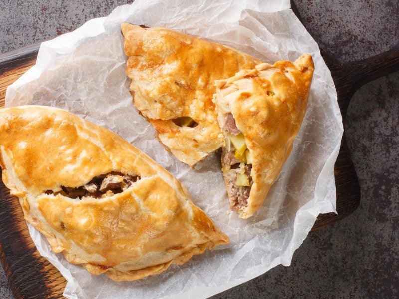 Ein dunkles Holztablett mit Cornish Pasty darauf.