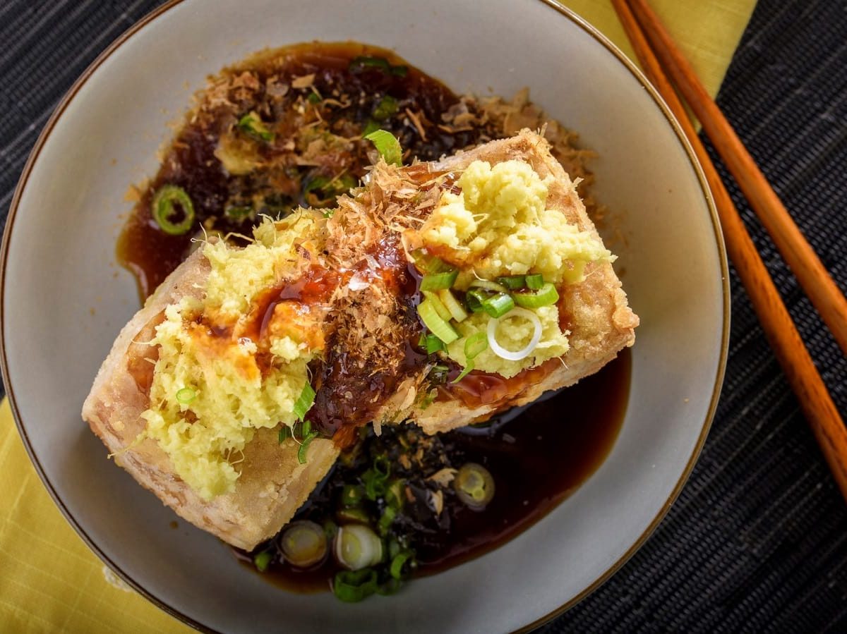 Ein Teller mit Agedashi Tofu neben einem Paar Stäbchen.