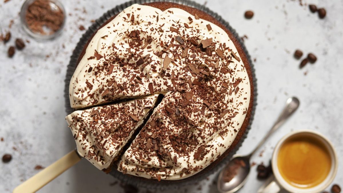 Irish-Coffee-Kuchen mit Schlagsahne und geriebener Schokolade in einer Form. Daneben steht eine Tasse Kaffee.