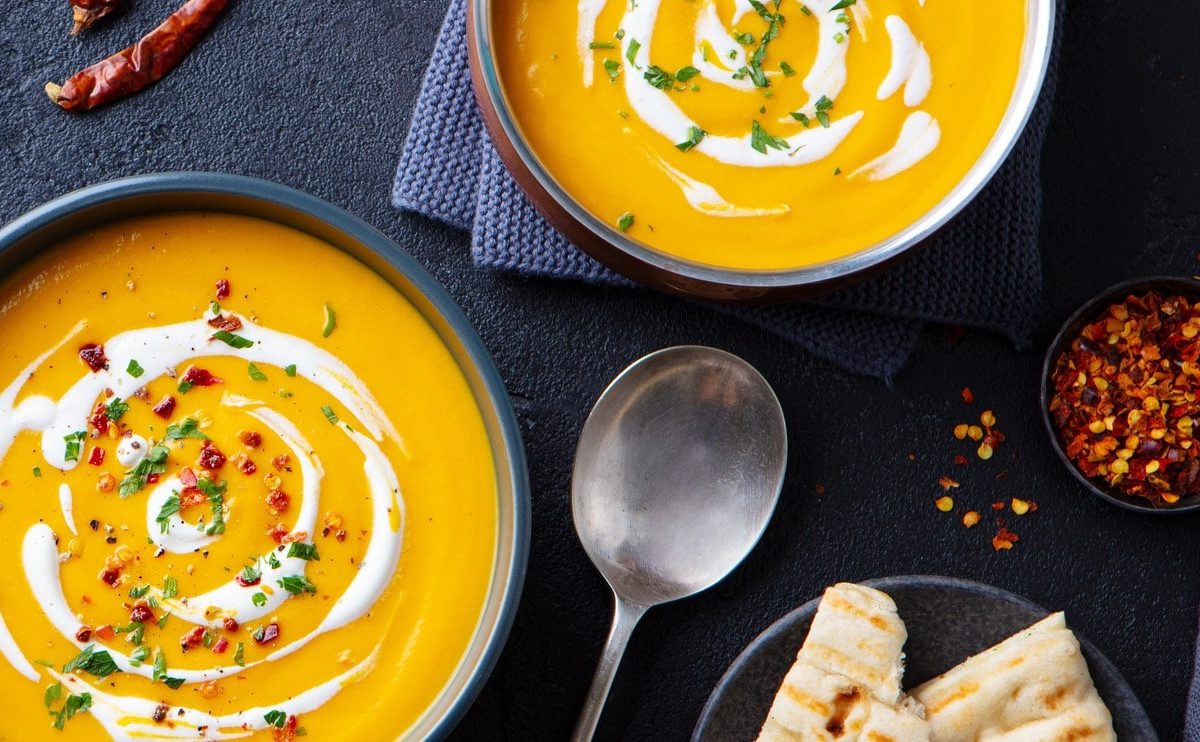 Zwei Teller voll Kürbissuppe mit Erdnussbutter und Kokosmilch auf dunklem Untergrund.