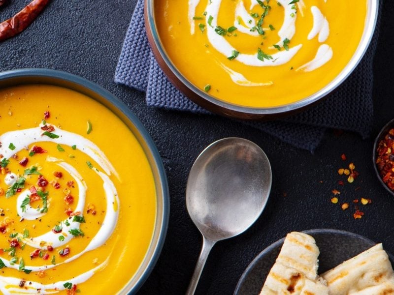 Zwei Teller voll Kürbissuppe mit Erdnussbutter und Kokosmilch auf dunklem Untergrund.