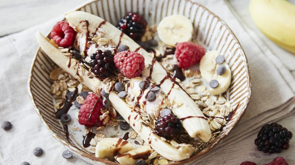 Ein runder Teller mit Banana-Split mit Frozen Quark und Müsli.