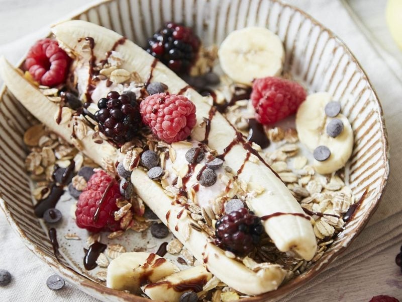 Ein runder Teller mit Banana-Split mit Frozen Quark und Müsli.