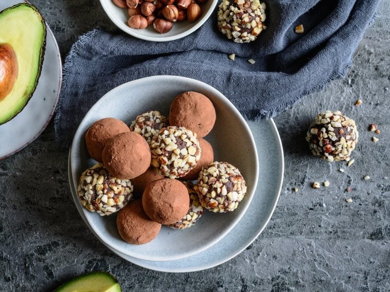 Eine hellblaue Schüssel mit Avocado-Schokoladen-Trüffeln neben frischer Avocado.