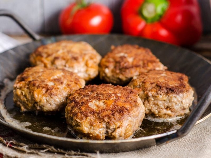 Draufsicht auf eine Pfanne mit 5 bayerischen Fleischpflanzerl. Im Hintergund liegen 2 rote Paprika.