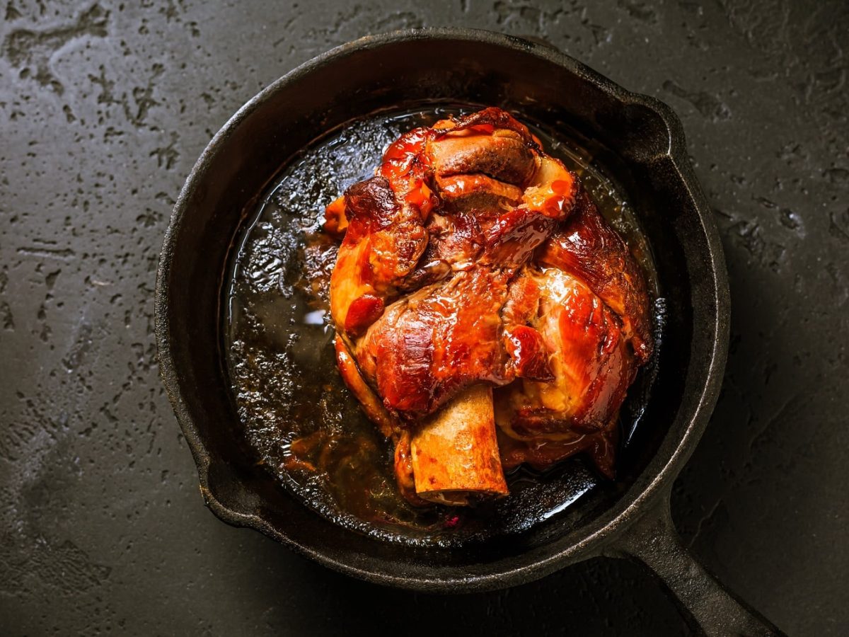 Eine bayerische Schweinshaxe in einer gusseisernen Pfanne in der Draufsicht.