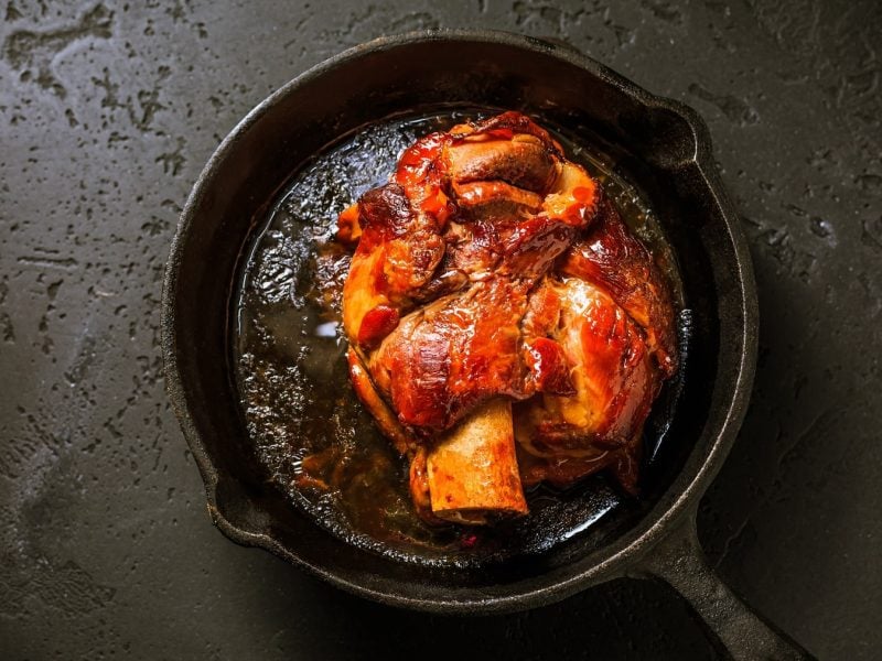 Eine bayerische Schweinshaxe in einer gusseisernen Pfanne in der Draufsicht.