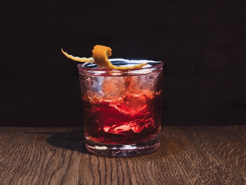 Der Boulevardier Cocktail auf einem Holztisch mit dunklem Hintergrund.