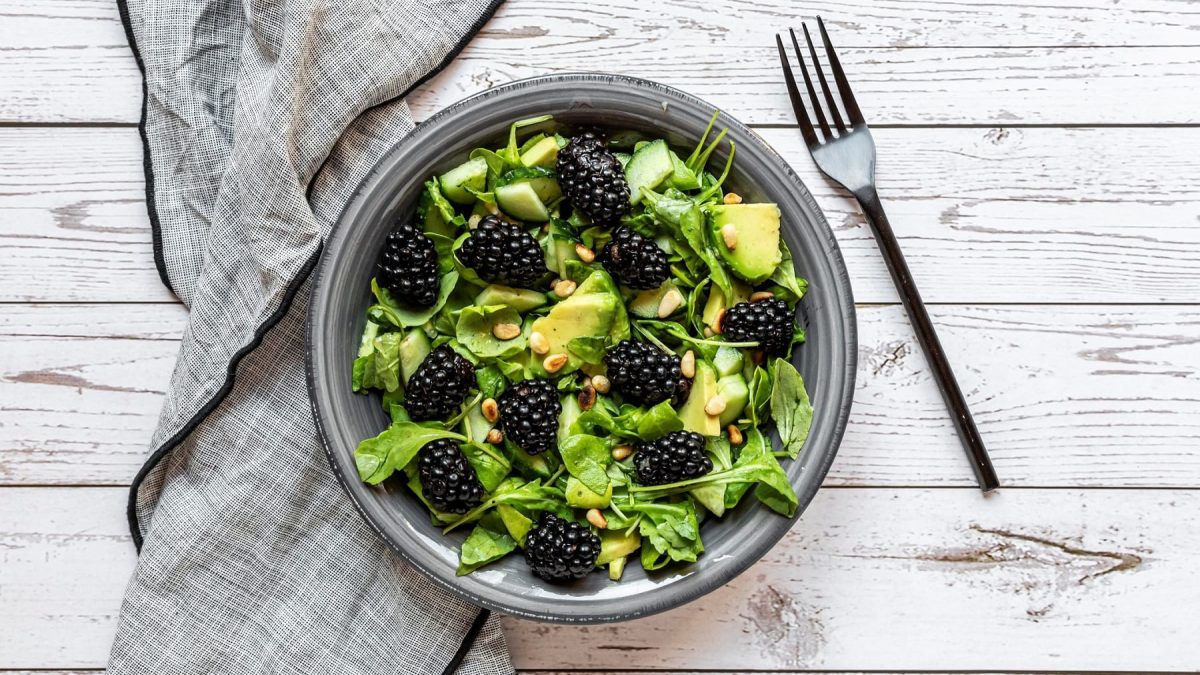 Eine Schale Brombeer-Avocado-Salat in der Draufsicht, daneben eine Gabel und eine Serviette aus Stoff.