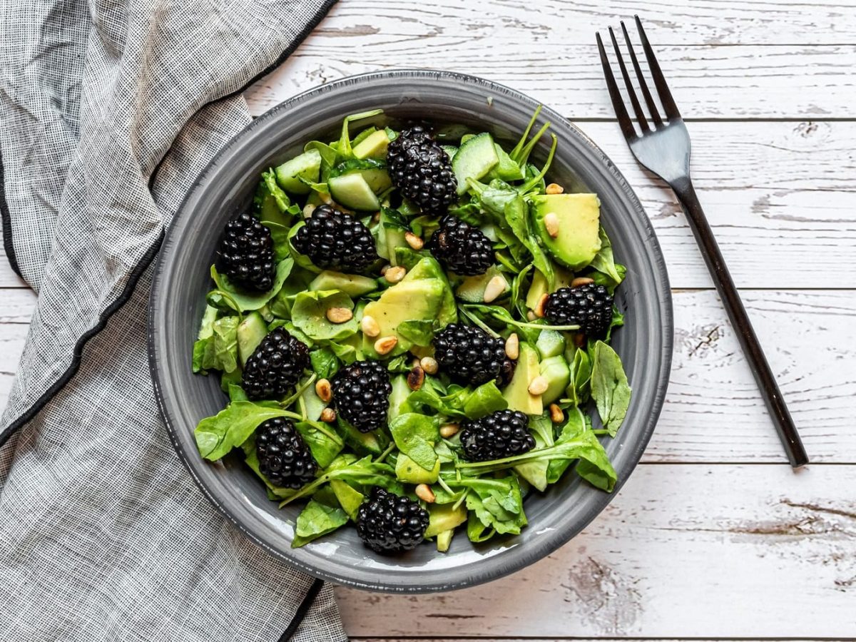 Eine Schale Brombeer-Avocado-Salat in der Draufsicht, daneben eine Gabel und eine Serviette aus Stoff.