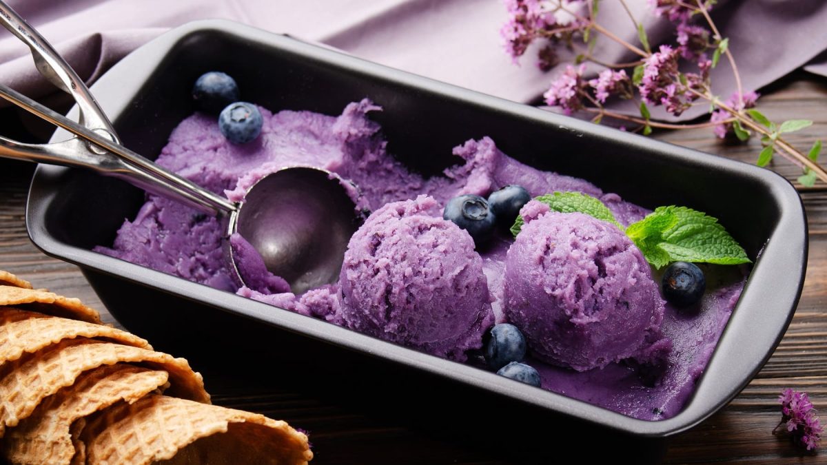 Eine Kastenform mit Brombeer-Nicecream, darauf Eiskugeln und ein Eisportionierer.