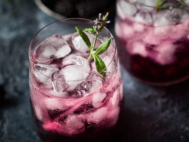 Zwei Gläser mit dem violetten Cocktail auf einem dunklen Untergrund.