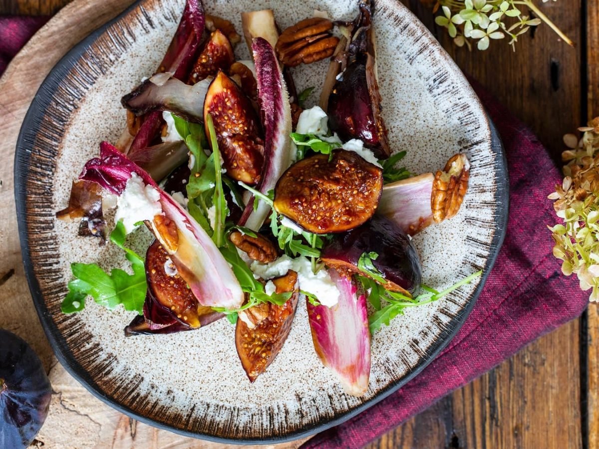 Chicoréesalat mit karamellisierten Feigen und Rucola sowie Feta auf einem Teller in der Draufsicht.