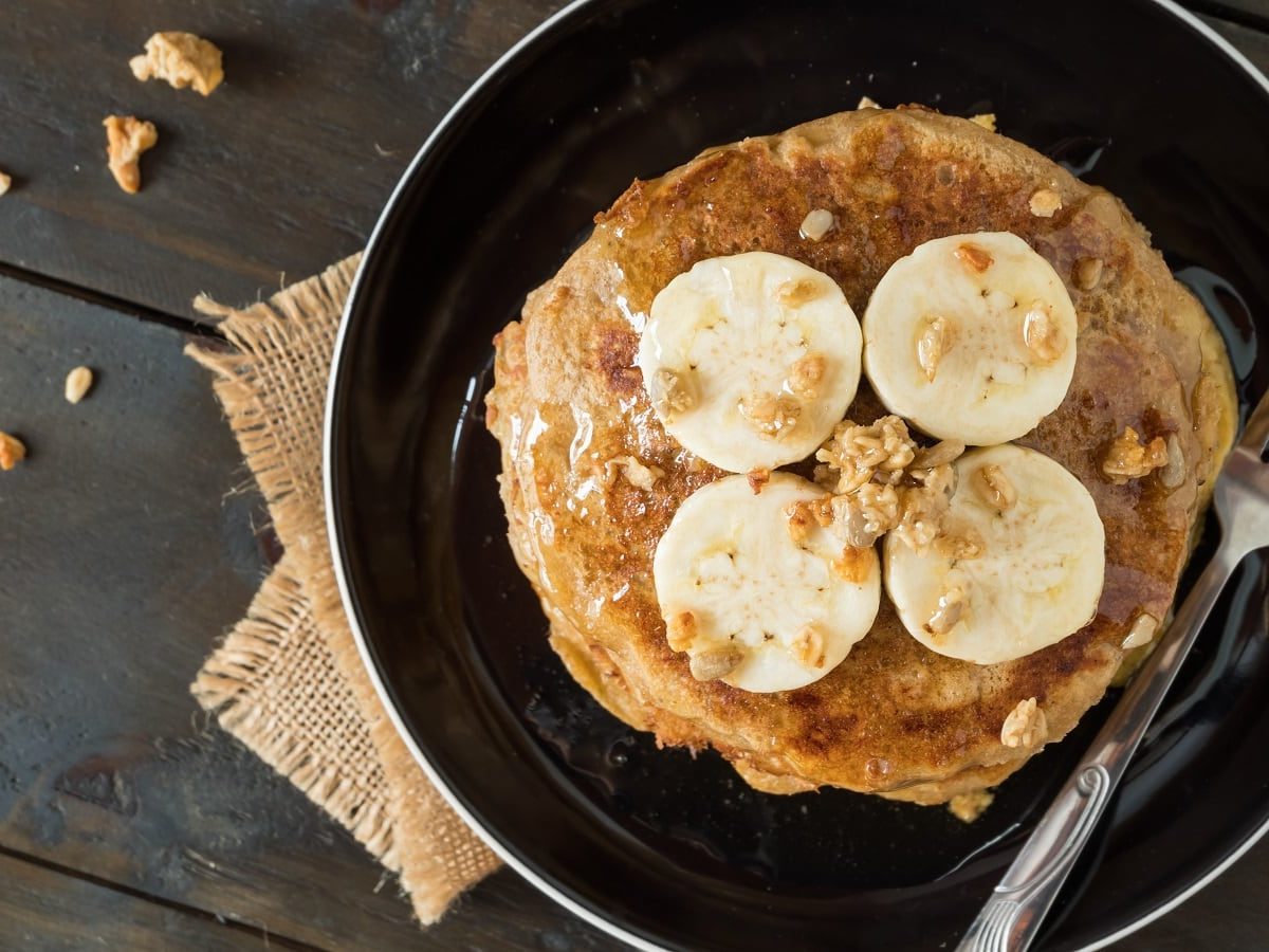 Ein schwarzer Teller mit Bananen-Pancakes auf einem braunen Tuch.