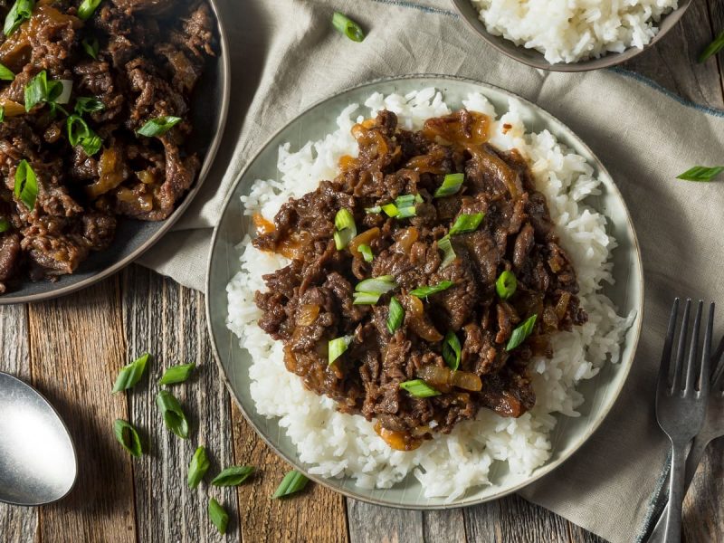 Ein weißer Teller mit Reis und Bulgogi auf einem grauen Tuch.