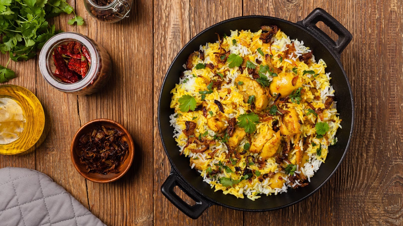 Ein schwarzer Topf mit Chicken Biryani auf einem Holztisch.