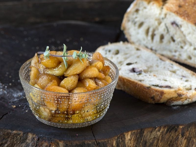 Ein Glas mit Knoblauch-Konfit neben Brot auf einer Baumscheibe