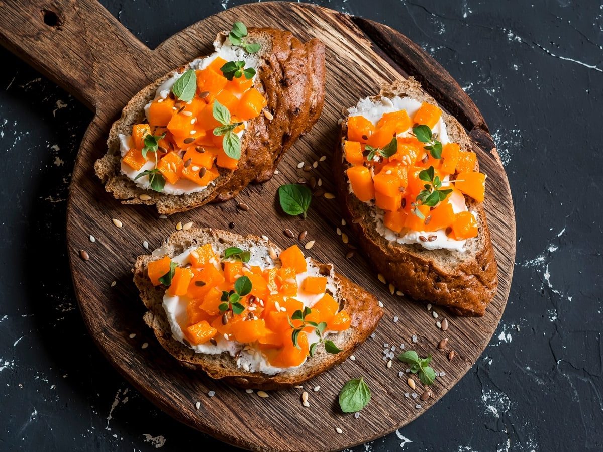 Ein Holzbrett mit Kürbis-Bruschetta mit Ziegenkäse darauf.