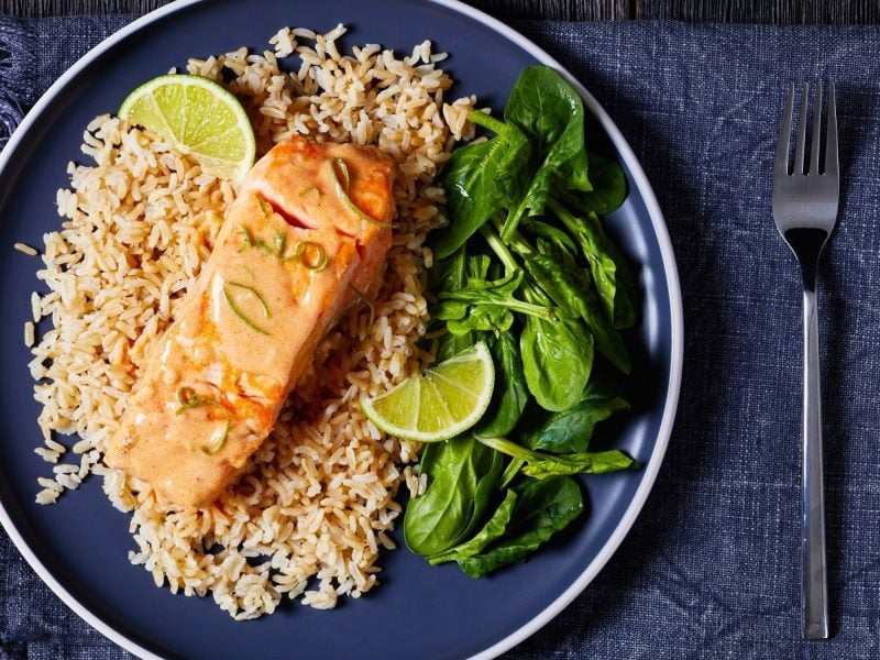 Ein dunkler Teller gefüllt mit Lachs in Kokos-Limetten-Sauce.