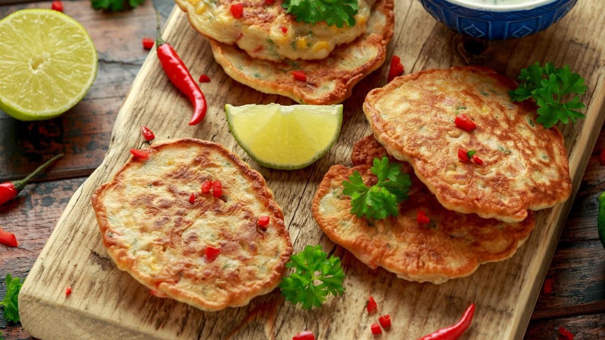 Ein Holzbrett mit Maispuffer mit Chili neben frischen Zutaten.