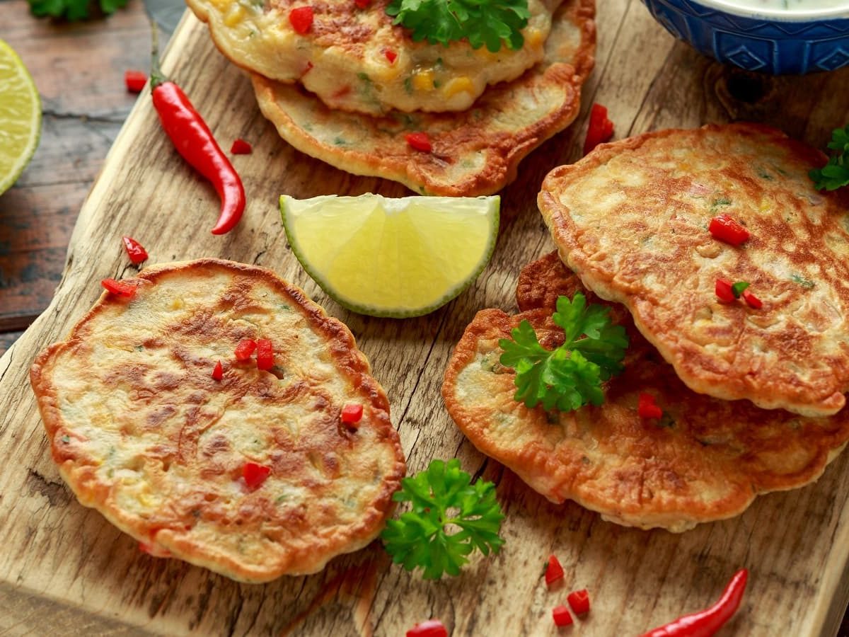 Ein Holzbrett mit Maispuffer mit Chili neben frischen Zutaten.