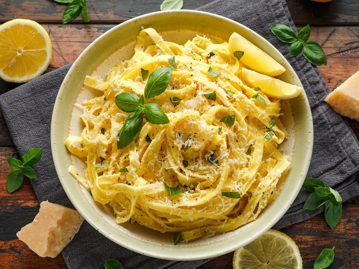 Ein runder weißer Teller mit Pasta mit Schmelzkäse neben Zitronenscheiben und Käseblocken.